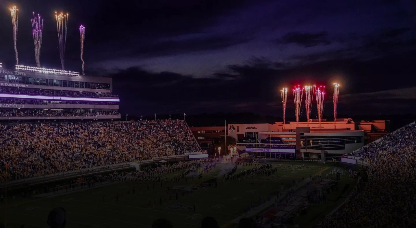 Fans fill a university stadium beneath game-day fireworks.